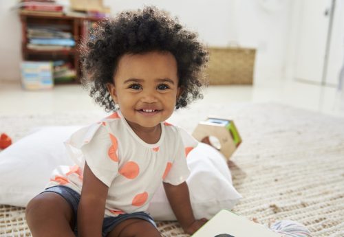 Portrait Of Happy Baby Girl Playing With Toys In Playroom